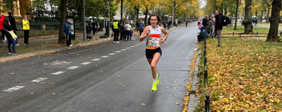Athletin mit Startnummer läuft auf nasser Straße im herbstlichen Park