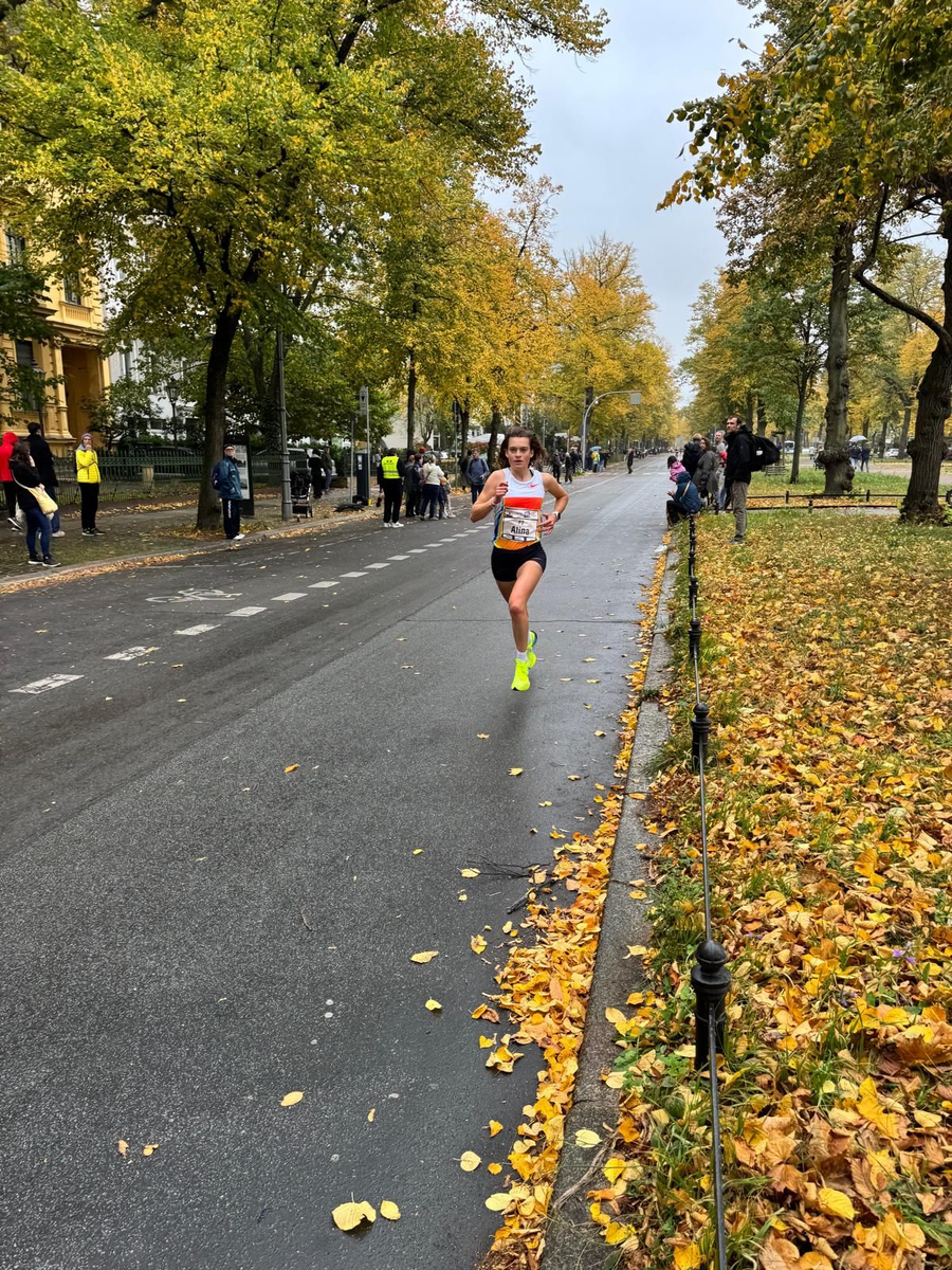 Athletin mit Startnummer läuft auf nasser Straße im herbstlichen Park
