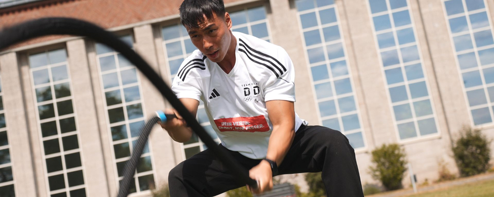 Person beim Battle-ropes Training im Freien vor Sporthalle