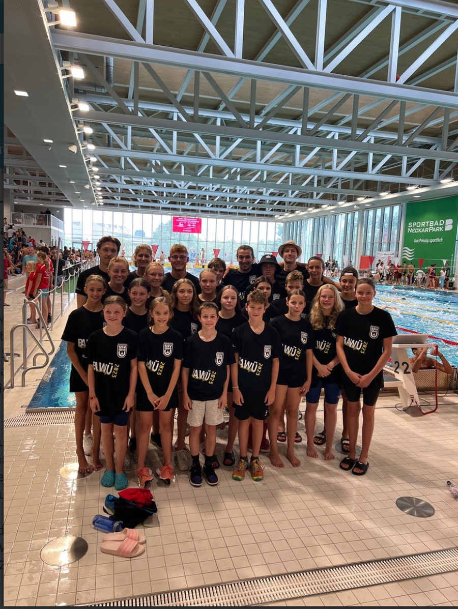 Jugendliches Schwimmteam posiert am Beckenrand in Hallenbad