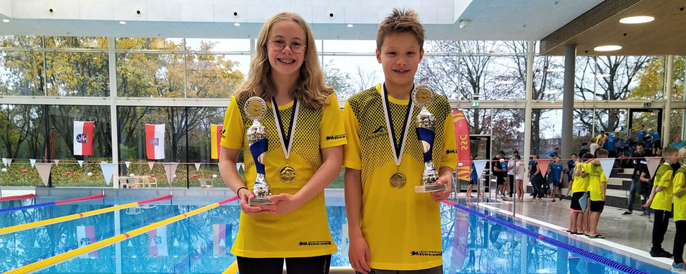 Zwei jugendliche Schwimmer auf Podest in gelben Trikots mit Pokalen am Pool