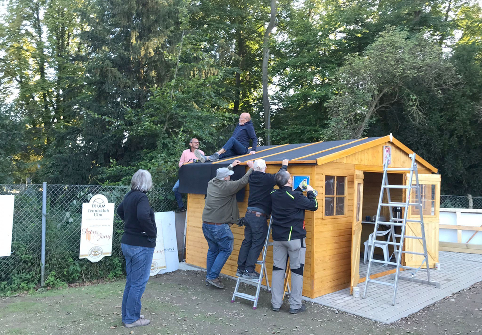 Mehrere Personen montieren Dach auf Holzschuppen