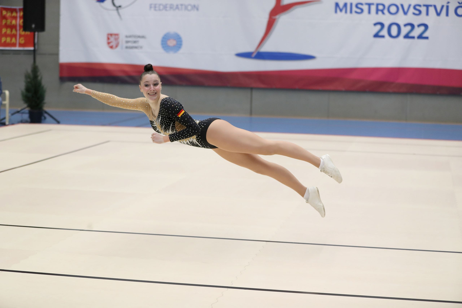 Aerobic-Athletin in schwarzem Wettkampfanzug springt quer über Matte