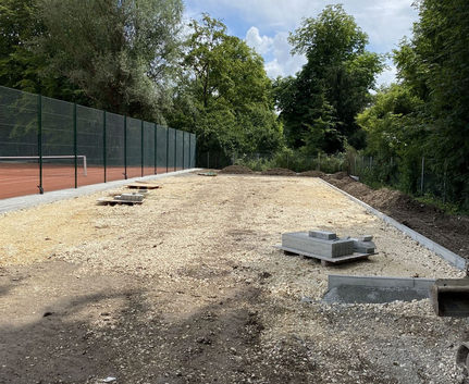 Baustelle mit Schotterunterbau, Paletten mit Betonplatten, Tennisplatzzaun links