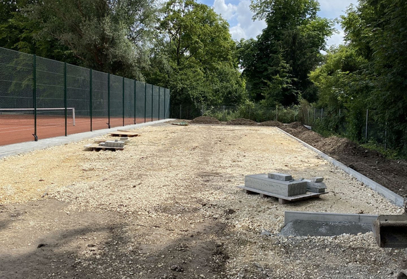 Baustelle mit Schotterunterbau, Paletten mit Betonplatten, Tennisplatzzaun links