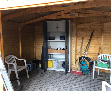 Innenraum eines Holzschuppens mit offenem Metallschrank Gartenwerkzeugen und zwei weißen Stühlen