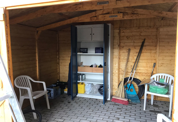 Innenraum eines Holzschuppens mit offenem Metallschrank Gartenwerkzeugen und zwei weißen Stühlen