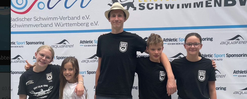 Fünf SSV Ulm Schwimmerinnen und Schwimmer lächelnd vor Sponsorenwand