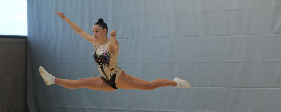 Aerobic-Sportlerin im weiten Spagat-Sprung während Wettkampf