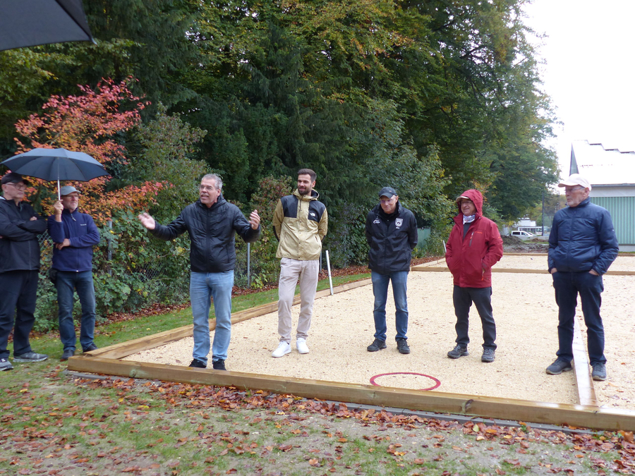 Männer auf Bouleplatz im Regen bei Eröffnungsfest einer gestikuliert