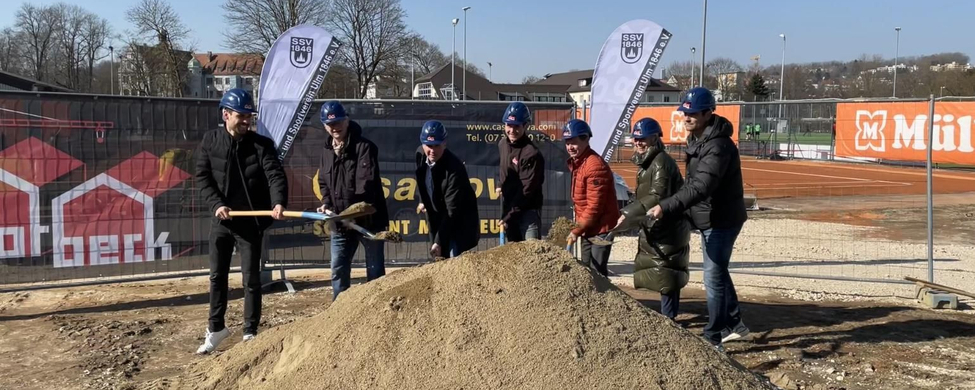 Sieben Personen mit blauen Helmen beim symbolischen Spatenstich