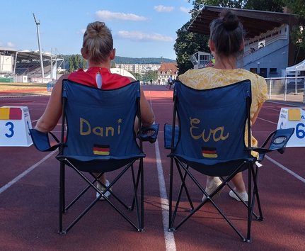Zwei Klappstühle auf Tartanbahn mit Aufschriften Dani und Eva und deutschen Flaggen