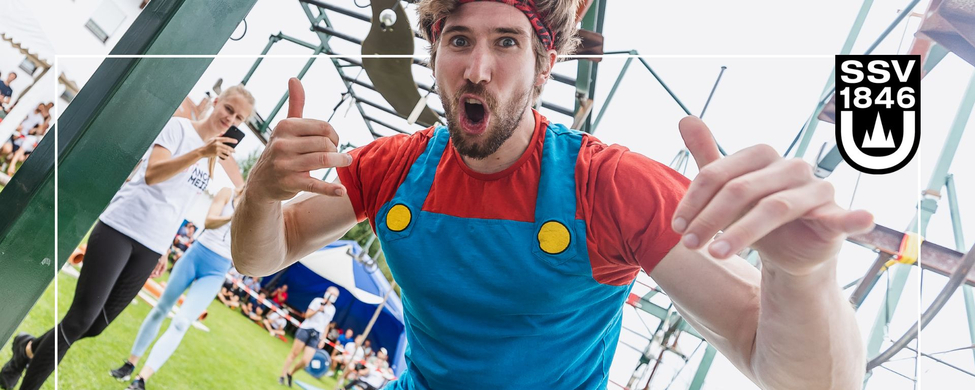 Teilnehmer jubelt vor Ninja Warrior Parcours Daumen hoch Zuschauer im Hintergrund