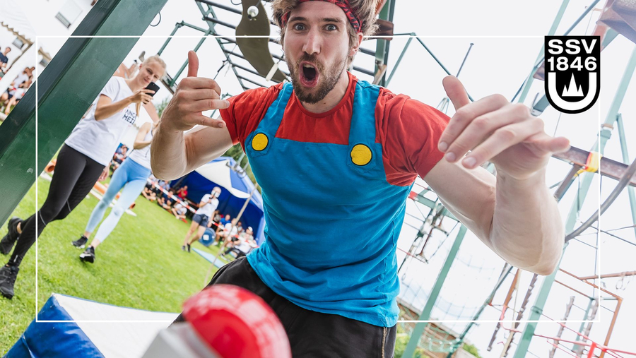 Teilnehmer jubelt vor Ninja Warrior Parcours Daumen hoch Zuschauer im Hintergrund