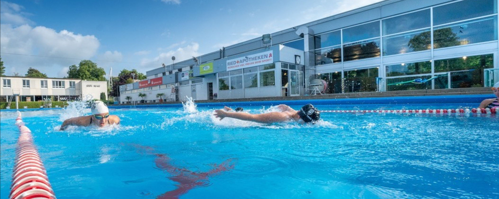 Zwei Schwimmer trainieren in benachbarten Bahnen eines Freibads