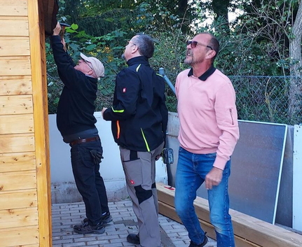 Drei Männer beim Aufbau einer Holzhütte am Bouleplatz
