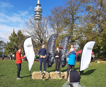 Podium mit drei Läuferinnen vor PeakPerformance Fahnen