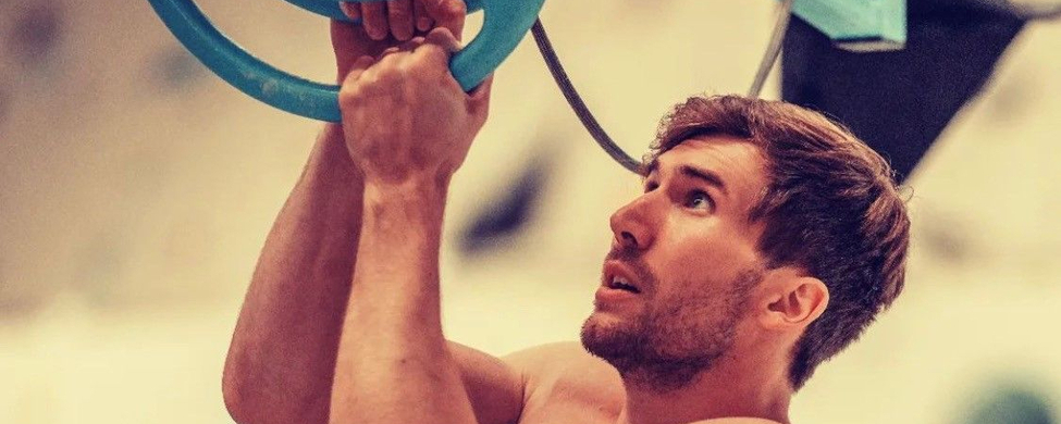 shirtloser Athlet am Ninja-Parkour hält sich an Ringen und schaut nach oben