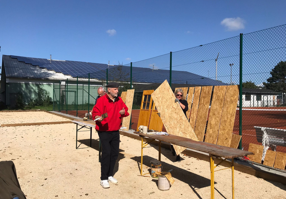 Drei Personen arbeiten an Holzplatten neben einem Tennisplatz