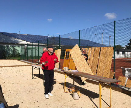 Drei Personen arbeiten an Holzplatten neben einem Tennisplatz