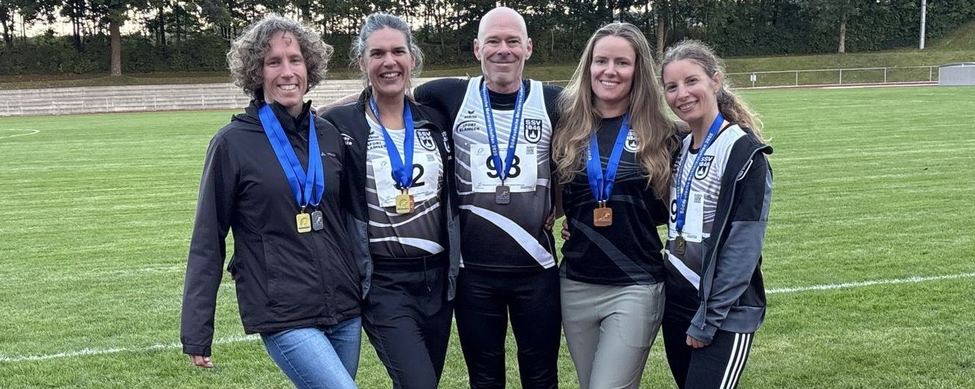 Gruppe aus vier Athletinnen und einem Athleten mit Medaillen auf Laufbahn