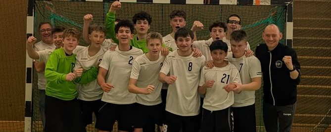 Männliche B-Jugend jubelnd vor Handballtor mit Trainern