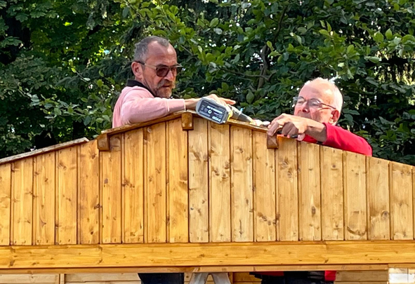 Two men assembling wooden shed roof with power drill