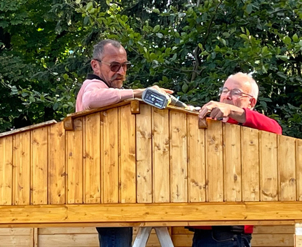 Two men assembling wooden shed roof with power drill