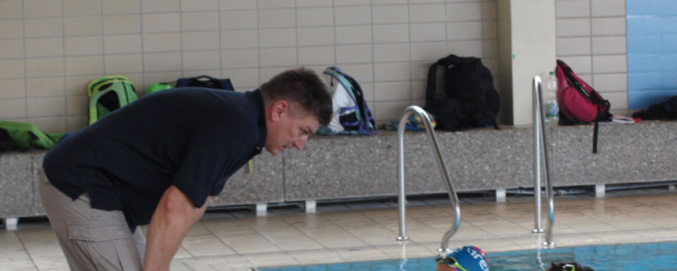 Trainer beugt sich zu drei jungen Schwimmern am Beckenrand