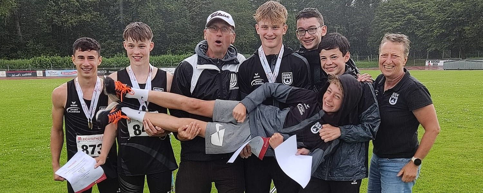 Hitze und Regen getrotzt: Die Ulmer Neunkampf-Riege U16-Athleten und Trainer tragen Teamkollegen vor Schild SCHÖNBUCHSTADION