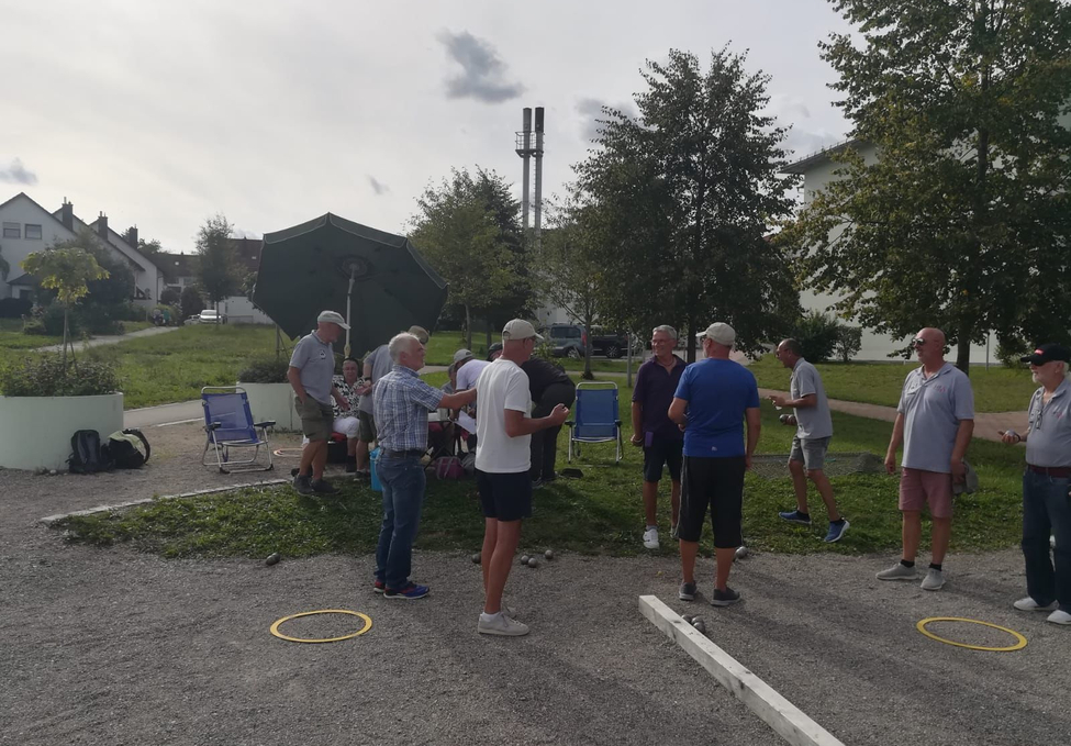 Mehrere Männer und Frauen spielen Boule auf Kiesplatz im Park