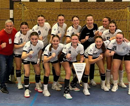 Weibliche Jugendhandballmannschaft jubelnd vor Tor mit Wimpel