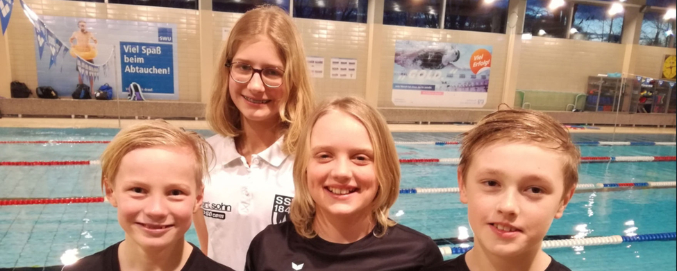 Vier junge Schwimmer lächelnd in SSV 1846 Shirts vor Schwimmbecken