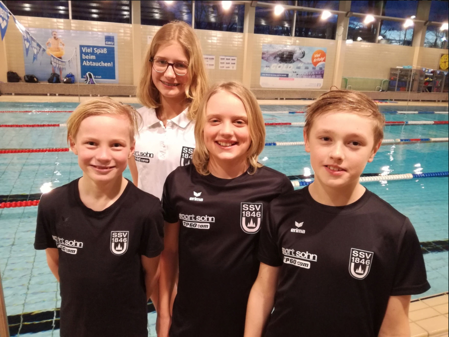 Vier junge Schwimmer lächelnd in SSV 1846 Shirts vor Schwimmbecken