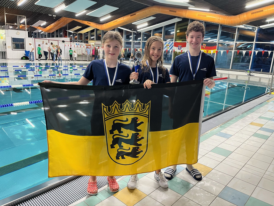 Drei jugendliche Schwimmer mit Medaillen und Flagge Baden-Württemberg am Beckenrand