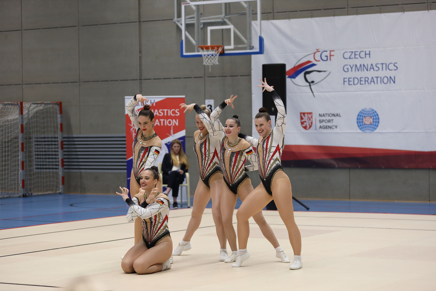Fünf Gymnastinnen in synchroner Gruppenroutine vor Czech Gymnastics-Banner