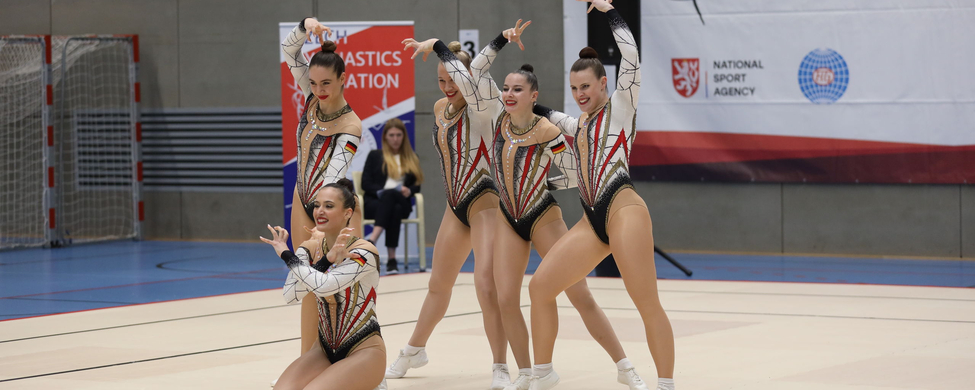 Fünf Gymnastinnen in synchroner Gruppenroutine vor Czech Gymnastics-Banner