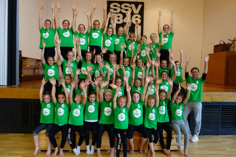 Lachende Mädchen in grünen T-Shirts mit erhobenen Händen beim Sommercamp