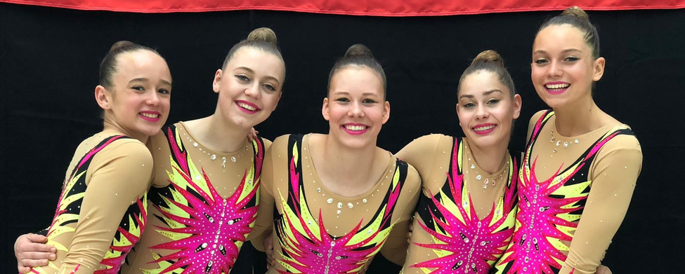 Fünf Aerobic-Athletinnen in pink-gelben Trikots lächelnd Arm in Arm