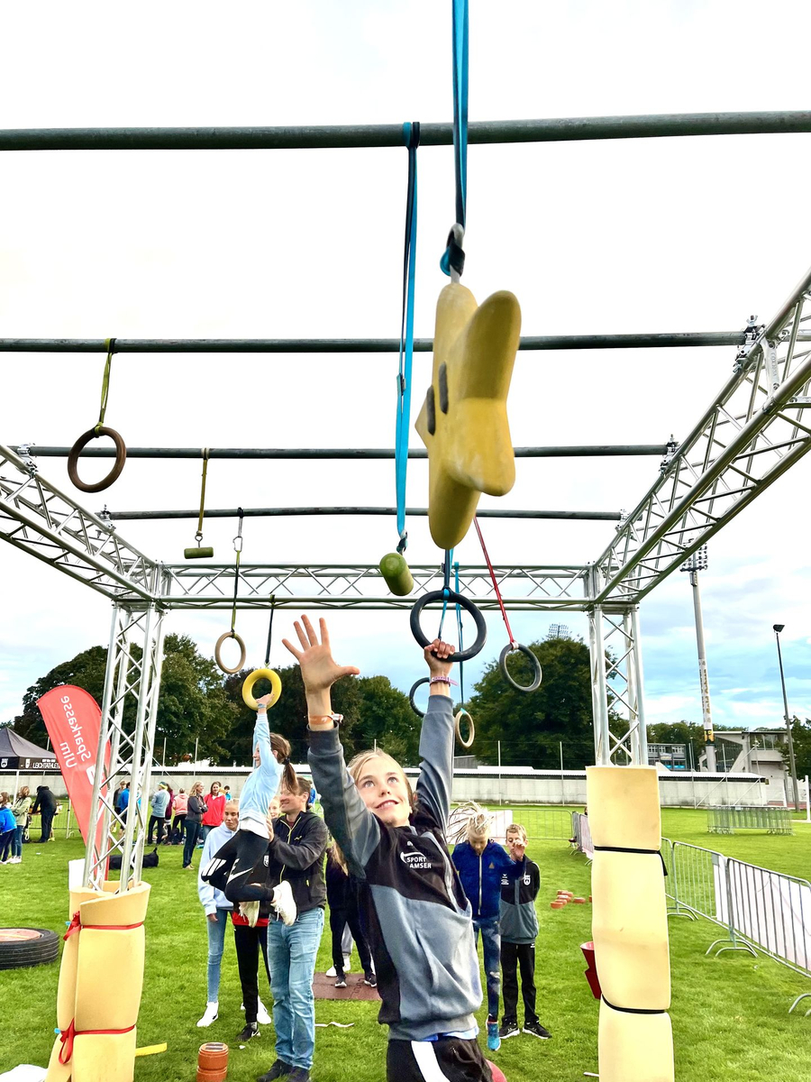 Mädchen greift nach Ringen am Ninja Parcours vor Zuschauern