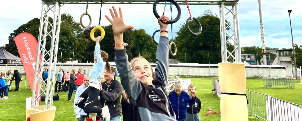 Mädchen greift nach Ringen am Ninja Parcours vor Zuschauern