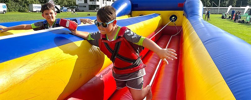 Zwei Kinder auf farbigem aufblasbarem Hindernis, eines mit Sonnenbrille