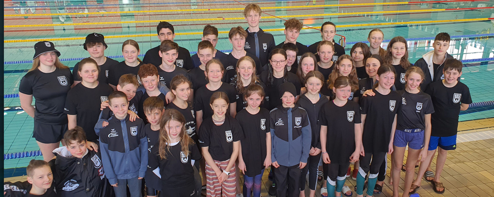 Ulmer Schwimmteam in Vereinskleidung lächelnd am Beckenrand