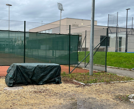 Green tarp covering equipment by fenced tennis court