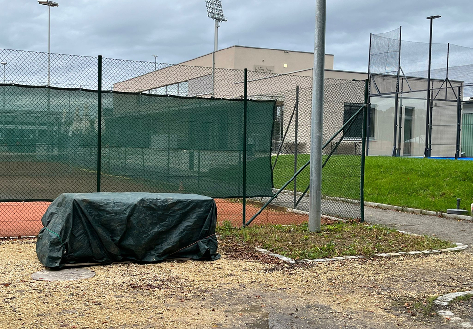 Green tarp covering equipment by fenced tennis court