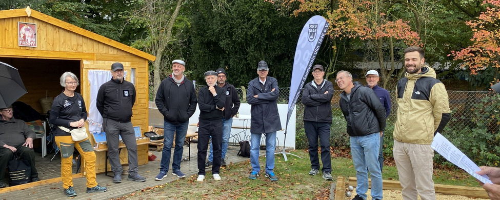 Erwachsene Gruppe steht vor Holzhütte und Fahne im Herbst