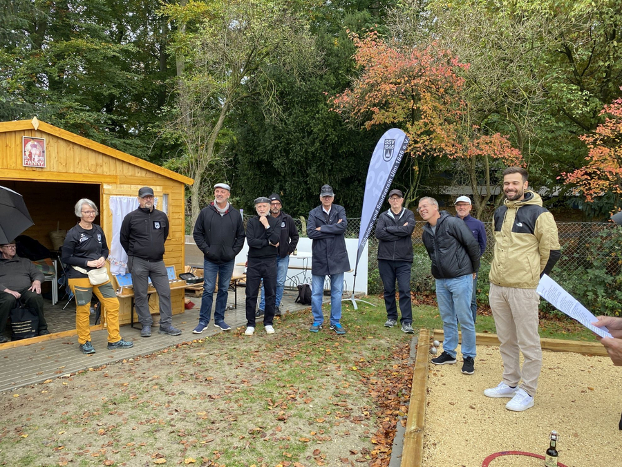 Erwachsene Gruppe steht vor Holzhütte und Fahne im Herbst