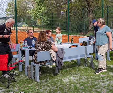 Mehrere Erwachsene und ein Mädchen an Tisch mit Bänken neben Tennisplatz