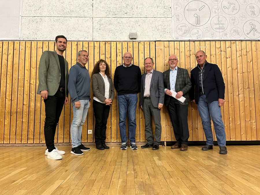 Sieben Personen stehen in Sporthalle vor Holzverkleidung