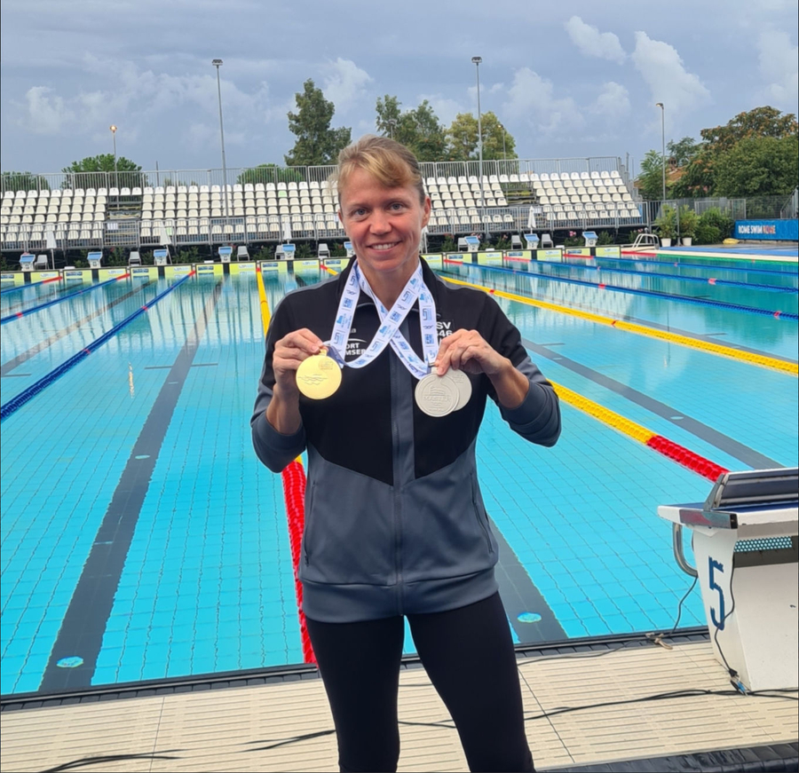 Schwimmerin am Beckenrand hält Gold- und Silbermedaille